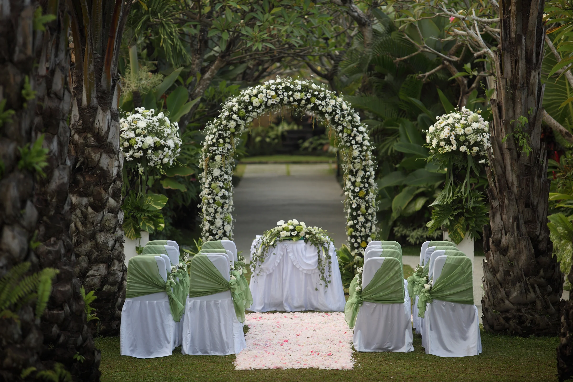 A white floral ceremony arch framed by the tropical Mahagiri garden